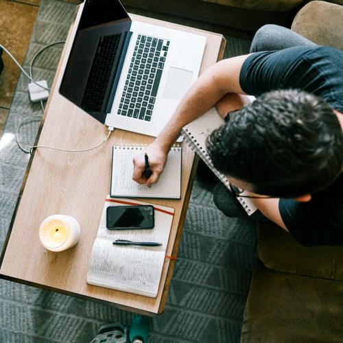 man in black t-shirt sitting at the table using macbook pro